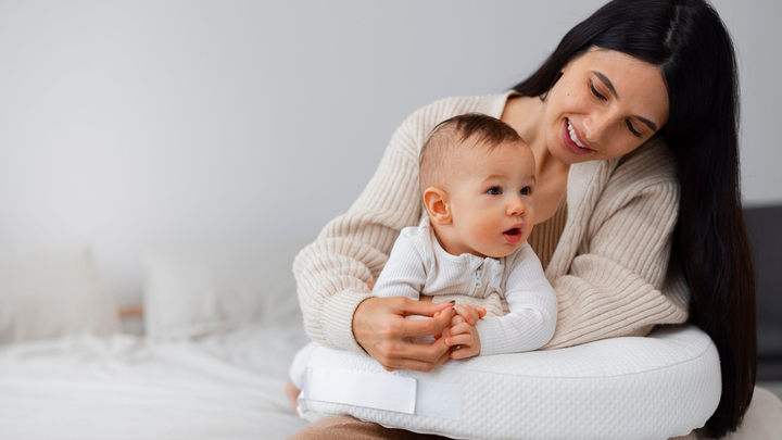 Mutter hält ihr Baby auf einem Stillkissen im Arm und schaut es an